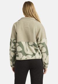 Polarowy sweter w beżowo-zielonym kamuflażu, z miękką teksturą, kołnierzykiem i naszywką na górnej części pleców.