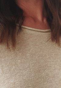 Béžový pletený svetr s texturovaným vzorem, širokým výstřihem a jemným žebrováním podél okrajů. Měkký, středně těžký materiál.