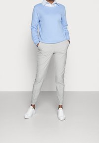 Lichtblauwe trui over een witte blouse, gecombineerd met grijze tapering broek en witte sneakers. Glad materiaal en minimalistisch design.