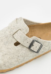 Wollen vilt slipper in lichtgrijs met een leren band en een metalen gespaccent. Heeft een gestructureerde bovenkant en een tan rubberen buitenzool.