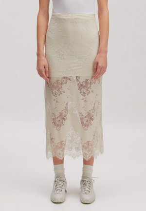 Cremefarbener Spitzen-Midirock mit Blumenmuster, getragen mit weißen Socken und Sneakers, kombiniert mit einem eng anliegenden weißen ärmellosen Top.