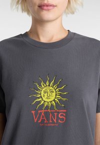 Szary bawełniany t-shirt z dużym żółtym słoneczkiem z twarzą. Logo "VANS" w wyrazistym czerwonym kolorze pod grafiką. Klasyczny okrągły dekolt.