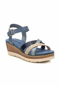 Sandalia de cuña con tiras de cuero azul y marrón, detalles perforados, correa de tobillo ajustable y plantilla acolchada sobre una suela ligera.