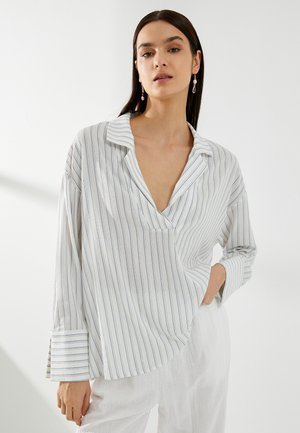 White long-sleeve shirt with blue vertical stripes, notch collar, and relaxed fit. Features rounded hem and wide cuffs. Soft fabric texture.