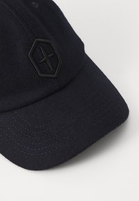 Navy wool cap featuring a textured surface, curved brim, and a prominent black hexagonal logo on the front.