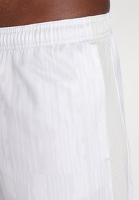 White Nike shorts with a textured fabric. Features an elastic waistband, mesh side panels, and a subtle tonal Nike logo pattern.