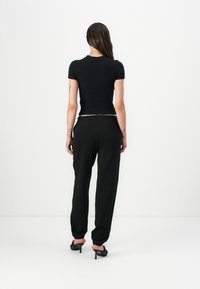 Svart, kortermet tettsittende topp kombinert med løse svarte joggebukser, som viser et cropped design og elastisk liv. Teksturert stoffdetalj synlig.