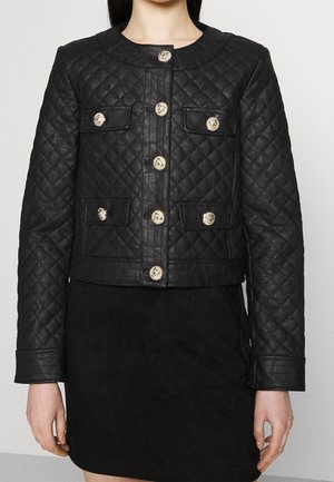 Veste matelassée noire avec des boutons dorés et quatre poches avant à rabat portée avec une jupe noire.