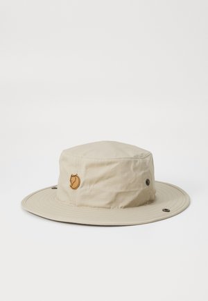 Chapeau seau beige en tissu léger, doté d'un large bord, d'un patch en cuir circulaire et d'œillets en métal pour la ventilation.