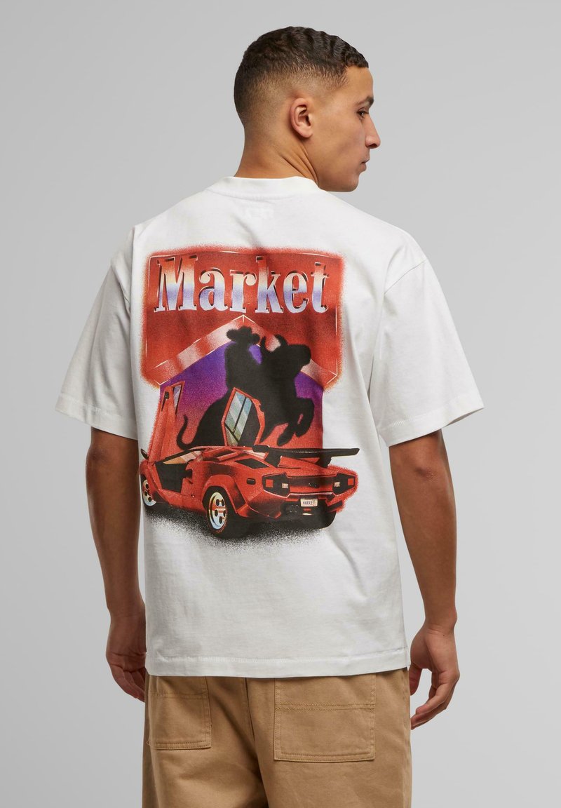 Camiseta blanca de algodón con un estampado gráfico de un coche rojo y una figura en silueta, con la palabra "Mercado" mostrada arriba en letras gruesas.