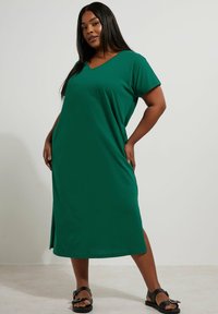 Zielona maksi sukienka z miękkiego materiału, z dekoltem w serek, krótkimi rękawami i bocznym rozcięciem. Połączona z czarnymi sandałami.