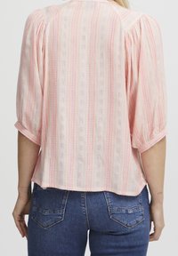 Blusa rosa chiaro, strutturata, con sottili righe verticali e maniche a sbuffo, dotata di scollo rotondo e orlo corto.