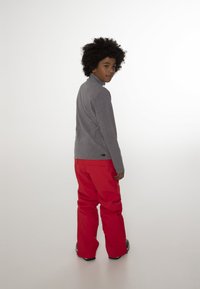 Grijze longsleeve shirt met een hoge kraag, gecombineerd met felrode, ruime broeken. Gestructureerde stof met een klein logo op de zoom van het shirt.
