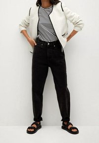 Veste blanche texturée avec bordure noire, t-shirt rayé noir et blanc, jean noir taille haute et sandales noires.