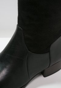 Stivale alla caviglia nero caratterizzato da una combinazione di pelle liscia e suede, con punta arrotondata e tacco a blocco impilato.