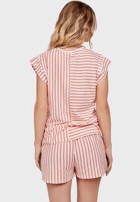 Top a maniche corte a righe e pantaloni abbinati in corallo e bianco. Tessuto morbido, vestibilità rilassata, con accenti plissettati sulle spalle e spacchi laterali.