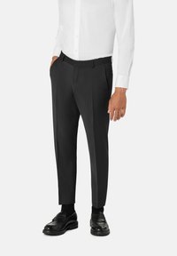 Pantalones negros a medida con frente plano, piernas entalladas y bolsillos laterales, combinados con una camisa blanca de botones y zapatos negros.