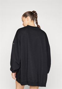 Sudadera negra de gran tamaño con mangas largas, puños acanalados y cuello redondo; hecha de una tela suave con una textura lisa.