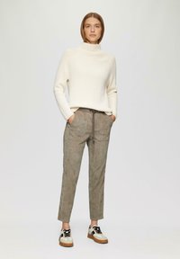 Crème ribbeltrui met col, gecombineerd met lichtbruine broek met trekkoord en witte sneakers met zwarte accenten. Eenvoudig, schoon ontwerp.