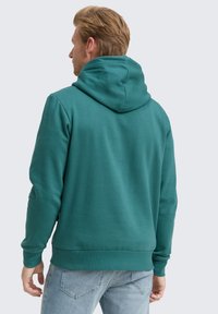 Sudadera con capucha, color teal, tejido suave, corte relajado, puños y dobladillo acanalados, presenta un diseño en la parte posterior con capucha y sin logotipos visibles.