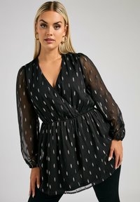 Blusa nera con maniche lunghe trasparenti, vita cinte e scollo a V. Presenta motivi argentati a forma di foglia su tutto il tessuto. Texture morbida.