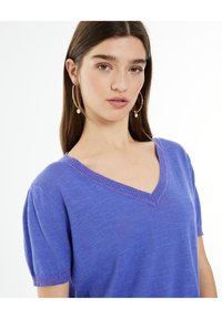 V-neck, short-sleeved top in vibrant purple. Soft texture with contrasting ribbed trim at neckline and sleeve edges. Features a relaxed fit.