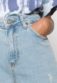 Shorts de mezclilla azul claro con dobladillo deshilachado, bolsillos delanteros, cierre de botón de metal y un sutil acabado desgastado en la tela.