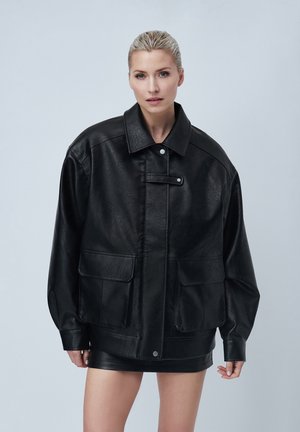 Black faux leather jacket with a wide collar, large front pockets, and a snap closure. Features a textured surface and oversized fit.