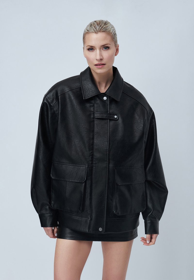 Veste en simili cuir noir avec un large col, de grandes poches avant et une fermeture à pression. Présente une surface texturée et une coupe ample.