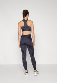 Black and grey tie-dye sports bra and leggings set, fitted design, smooth texture, paired with sneakers featuring a white sole and black accents.