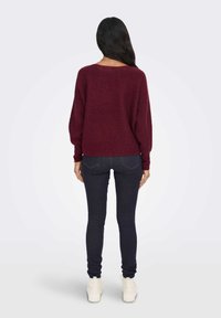 Bordový pletený svetr s volným střihem a širokými rukávy, kombinovaný s tmavými skinny džínami a bílými teniskami. Má zakulacený výstřih.