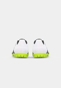 Chaussures de football blanches avec une bande noire et des semelles vert vif. Tige texturée avec un talon rembourré et un design incurvé.