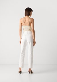 Beige pruhovaný top na tenkých ramínkách, spojený s bílými džínami s vysokým pasem a rovnými nohavicemi. Modelka má na sobě černé sandály na podpatku.