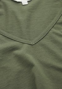 Vihreä oliivinvihreä puuvillapaita, jossa on V-neck-muotoilu, sileä pinta ja siisti ompelu kaula-aukon ja helman ympärillä.