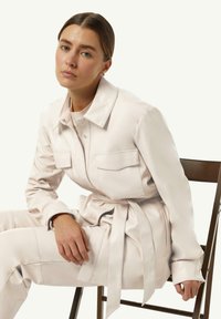 Jasnoróżowy zestaw z sztucznej skóry, składający się z kurtki na guziki z dwiema przednimi kieszeniami i wiązanym w pasie akcentem, zestawiony z dopasowanymi spodniami.