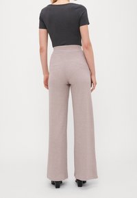 Pantalones de pierna ancha en suave tela beige con textura acanalada, diseño de cintura alta, presentados con una blusa negra ajustada de manga corta.