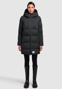 Black puffer coat with a hood, quilted design, front zipper, and side pockets. Worn over black leggings and knee-high black boots.