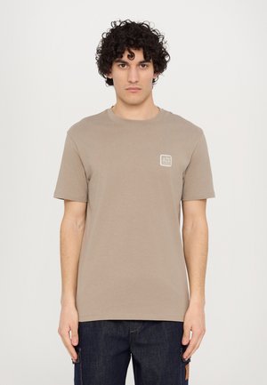 Kurzarm T-Shirt mit Rundhalsausschnitt aus taupefarbenem Baumwollstoff, mit einem kleinen quadratischen Logo in der oberen linken Ecke. Einfaches und minimalistisches Design.