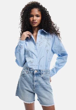Himmelblaues Hemd mit floralem Stickereien, kombiniert mit hochgeschnittenen Denim-Shorts mit ausgefransten Säumen.