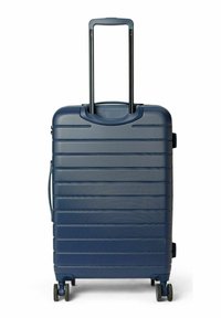 Valise rigide bleue avec lignes texturées, poignée rétractable et quatre roues. Dispose d'une poignée latérale pour un transport facile.