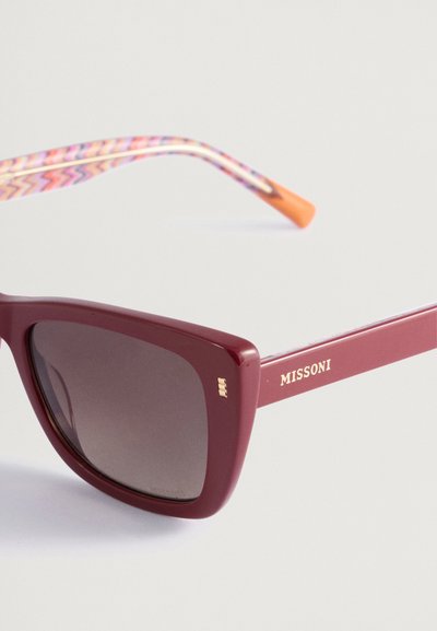 Óculos de sol quadrados bordeaux com lentes escuras, com hastes decoradas com um padrão colorido em zigue-zague e um logotipo dourado na têmpora.