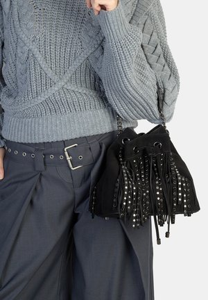 Borsa in suede nera con dettagli a frange e occhielli argentati. Abbinata a un maglione grigio lavorato a trecce e pantaloni scuri con cintura a fibbia.