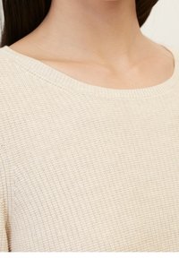 Pull beige tricoté avec un motif texturé, large encolure ronde et finitions côtelées. Gros plan sur le détail du tissu et du col.