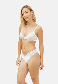 Ensemble de lingerie en dentelle blanche comprenant un bralette avec des bonnets en dentelle et des bretelles réglables, associé à une culotte ornée de dentelle assortie.