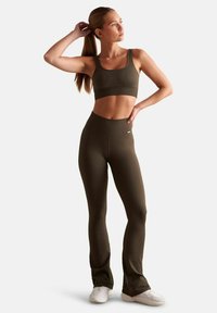 Ensemble de sport côtelé vert olive comprenant un crop top à encolure carrée et un legging évasé taille haute, associé à des baskets blanches.