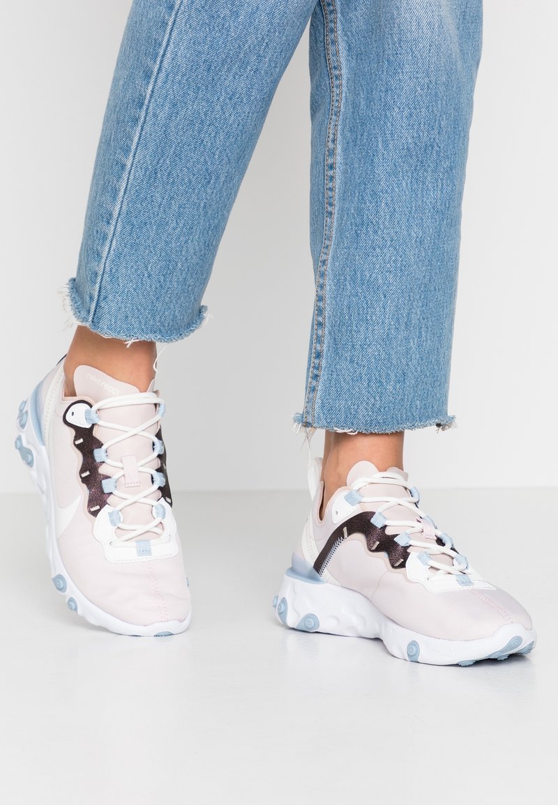 Ljust rosa sportskor med ett ventilerat övre, texturerade mörka accenter och en vit sula med blå detaljer. Bärs med avklippta jeans.