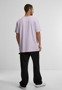 Tricou din bumbac lila deschis, cu o croială lejeră, mâneci scurte și decolteu rotund, asortat cu pantaloni cargo negri și adidași albi.