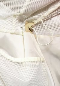Weißes Netzgewebe mit glatter Innenauskleidung, ausgestattet mit einem kleinen elastischen Verschluss und einer Netztasche entlang des Randes.