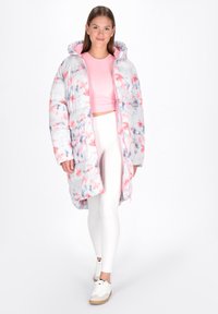 Polsterjacke in Weiß mit pinkem und blauem Batikmuster. Mit Kapuze und Fronttaschen. Getragen über einem pinken Crop-Top und weißen Leggings.