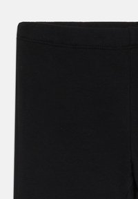 Leggings noirs en tissu lisse et extensible, avec une taille haute et des coutures renforcées. Le design est simple et sans couture.